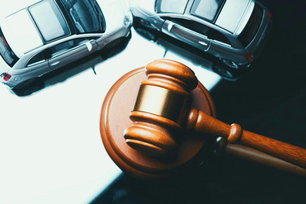 Close-up of a wooden judge’s gavel on a sound block with two cars positioned nearby, symbolizing a legal case or dispute involving a motor vehicle accident