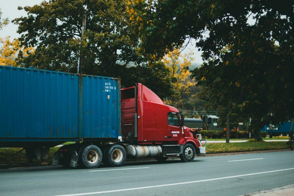 A large truck driving along a road, surrounded by trees and clear blue sky.